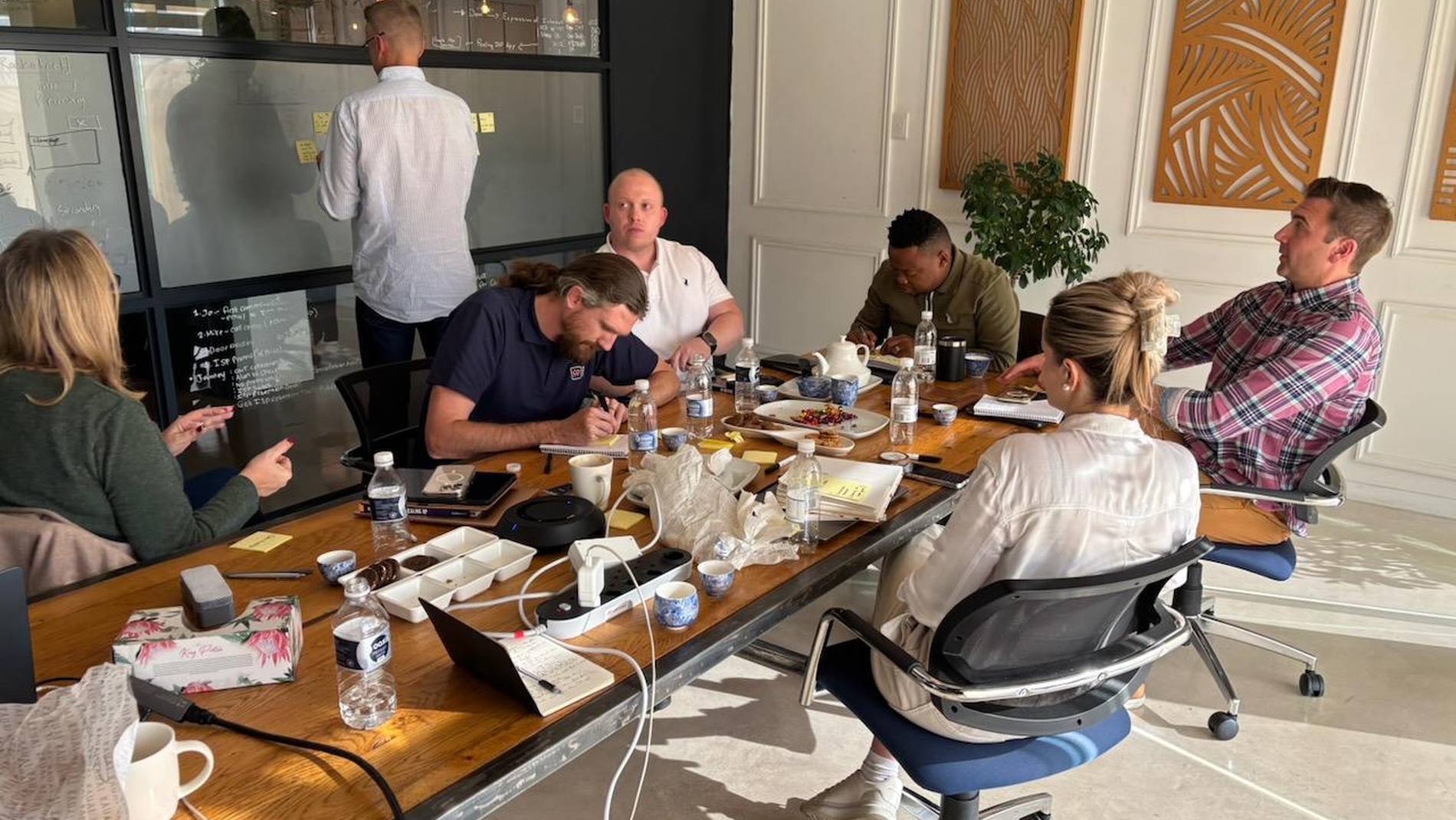 A ScaleUp working session around a boardroom table, the plan on the glass behind